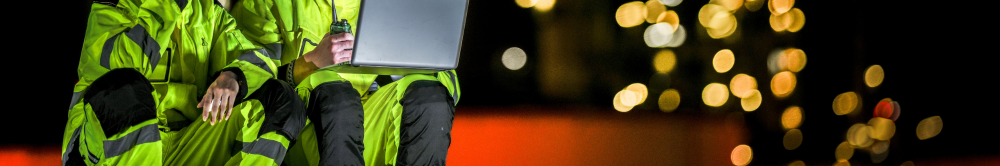 Mechanical engineering professionals in high-visibility PPE reviewing project mobilisation plans on-site during a large-scale UK industrial engineering project at night.